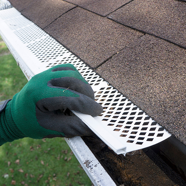 professional in green glove installing gutter guard on home